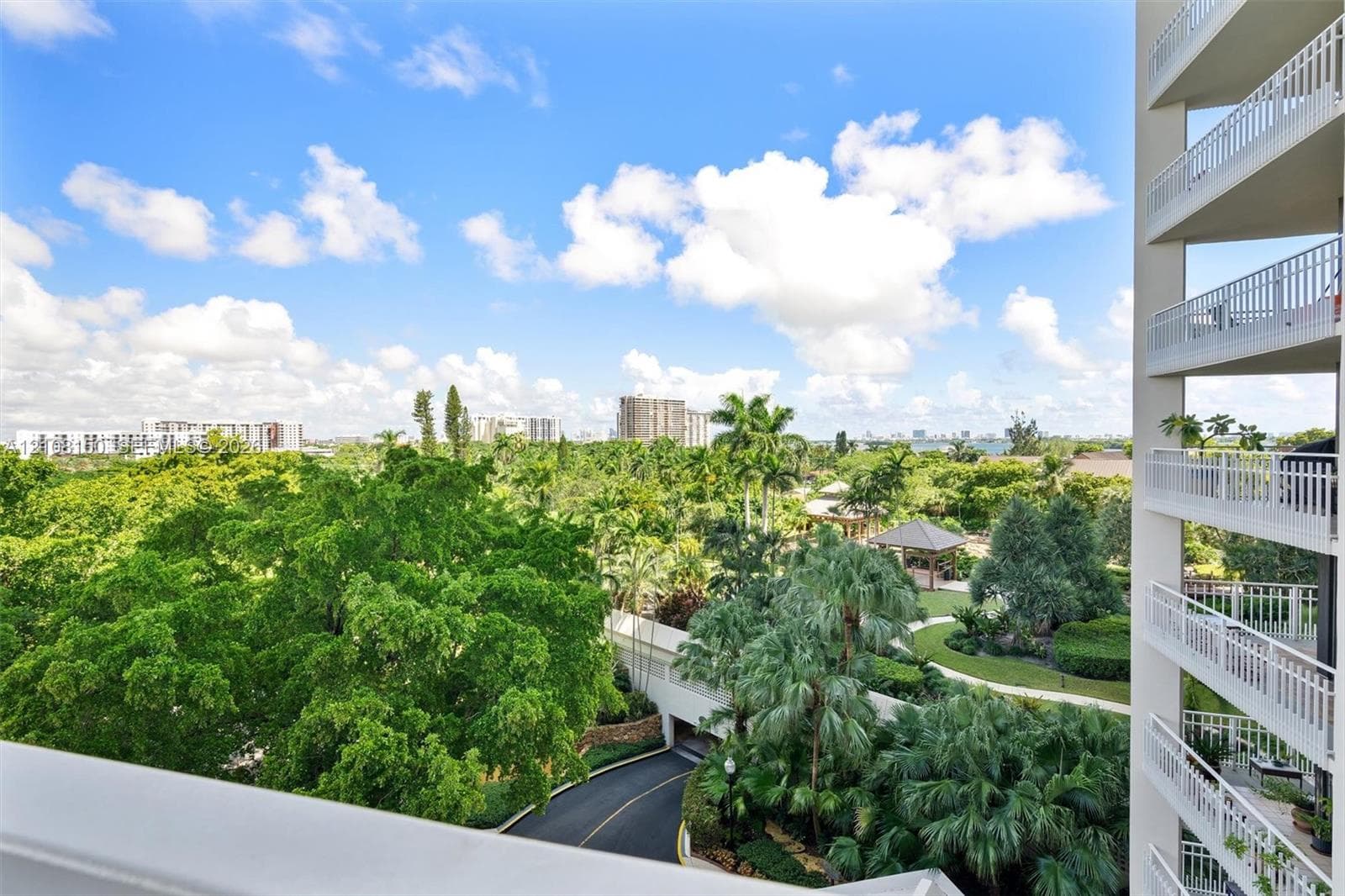 Elevated terrace featuring white metal railings, overlooking mature landscaping, palm trees, and paved roadways