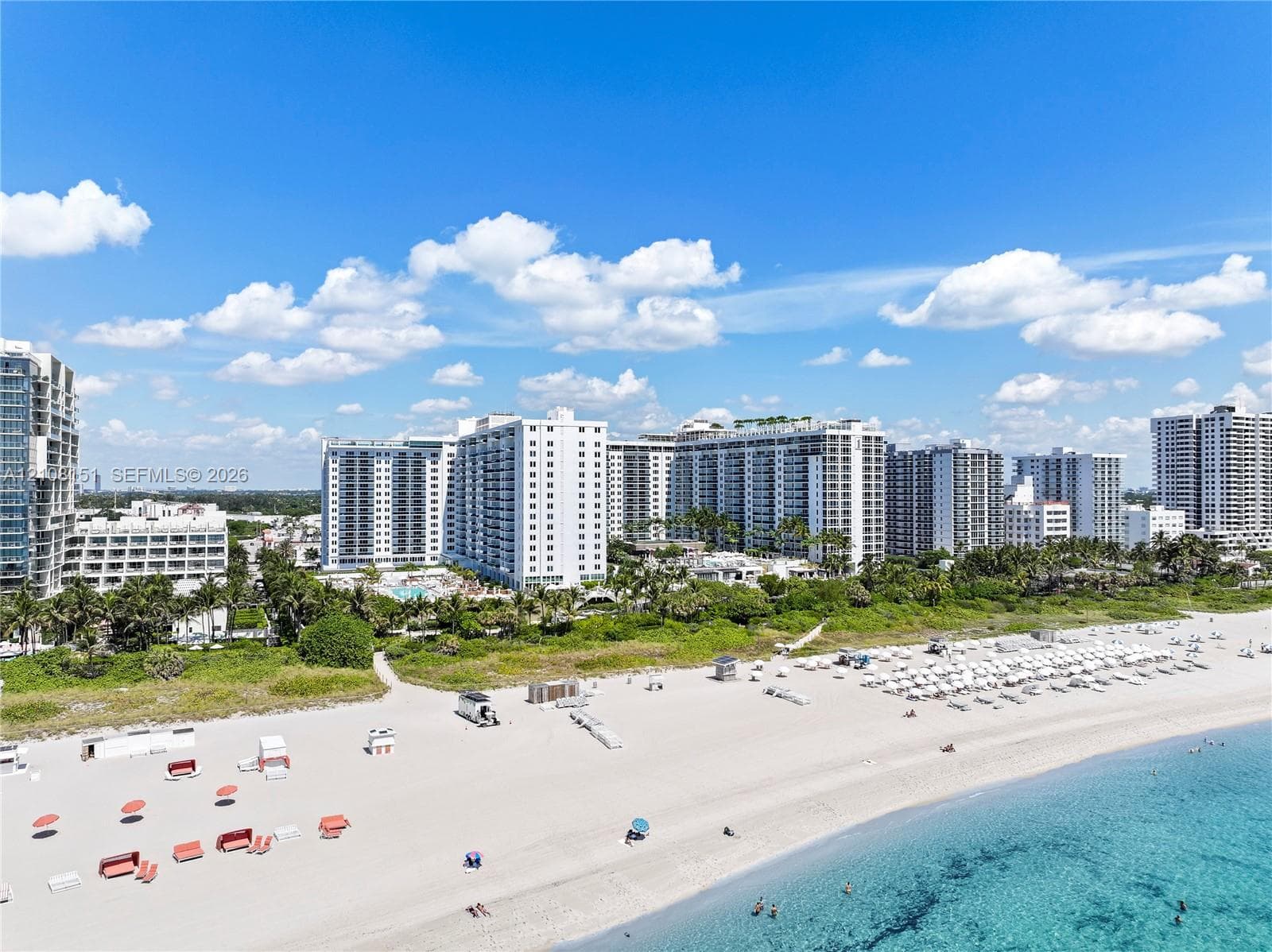 Aerial perspective of coastal high-rise development featuring direct beach access, sandy shoreline, and mature tropical landscaping