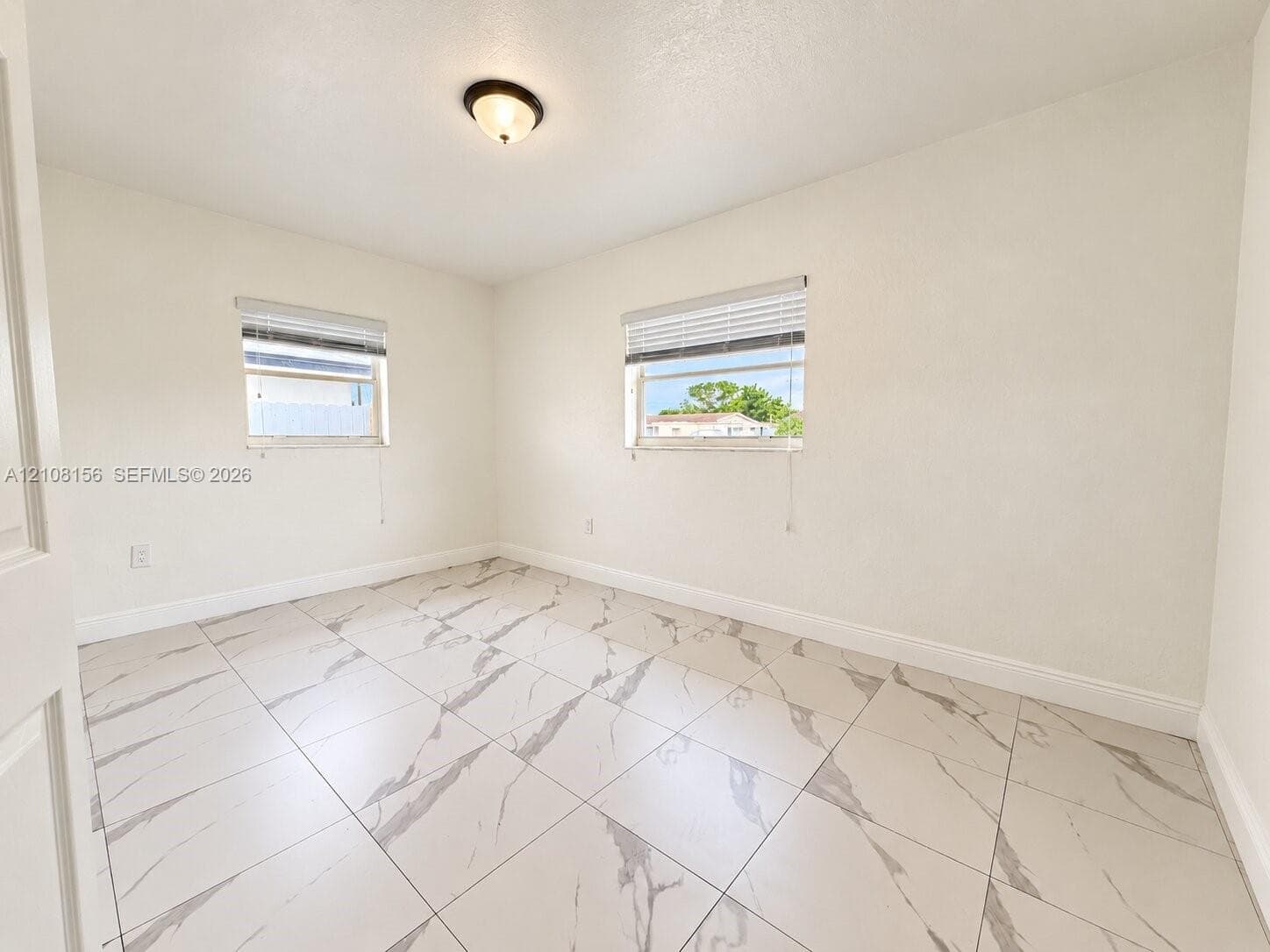 Room featuring large-format tile flooring with veining, two windows with horizontal blinds, and a centered flush-mount light fixture