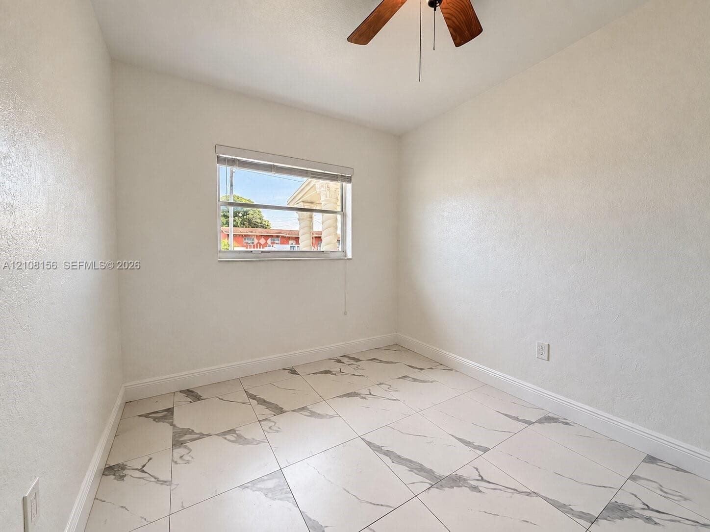 Room featuring large-format tile flooring with a neutral veined pattern, smooth wall finishes, a single-hung window, and a ceiling-mounted fan with wood-finish blades