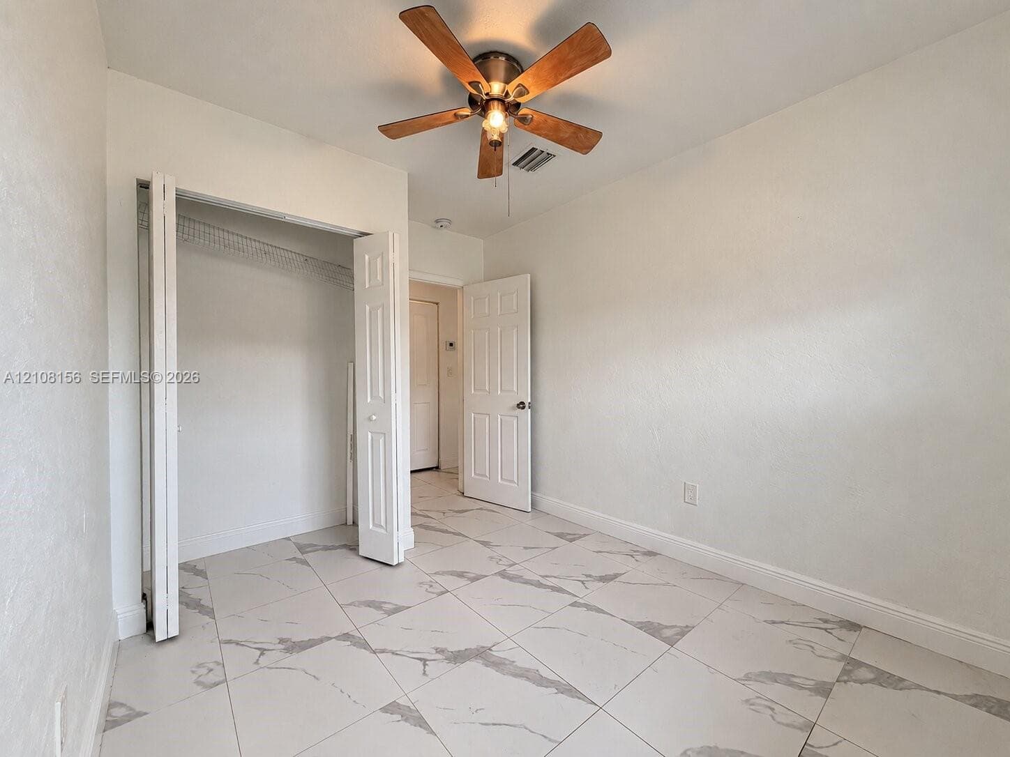 Large-format stone-patterned tile flooring, multi-panel interior door, bifold closet door, and ceiling fan with integrated lighting