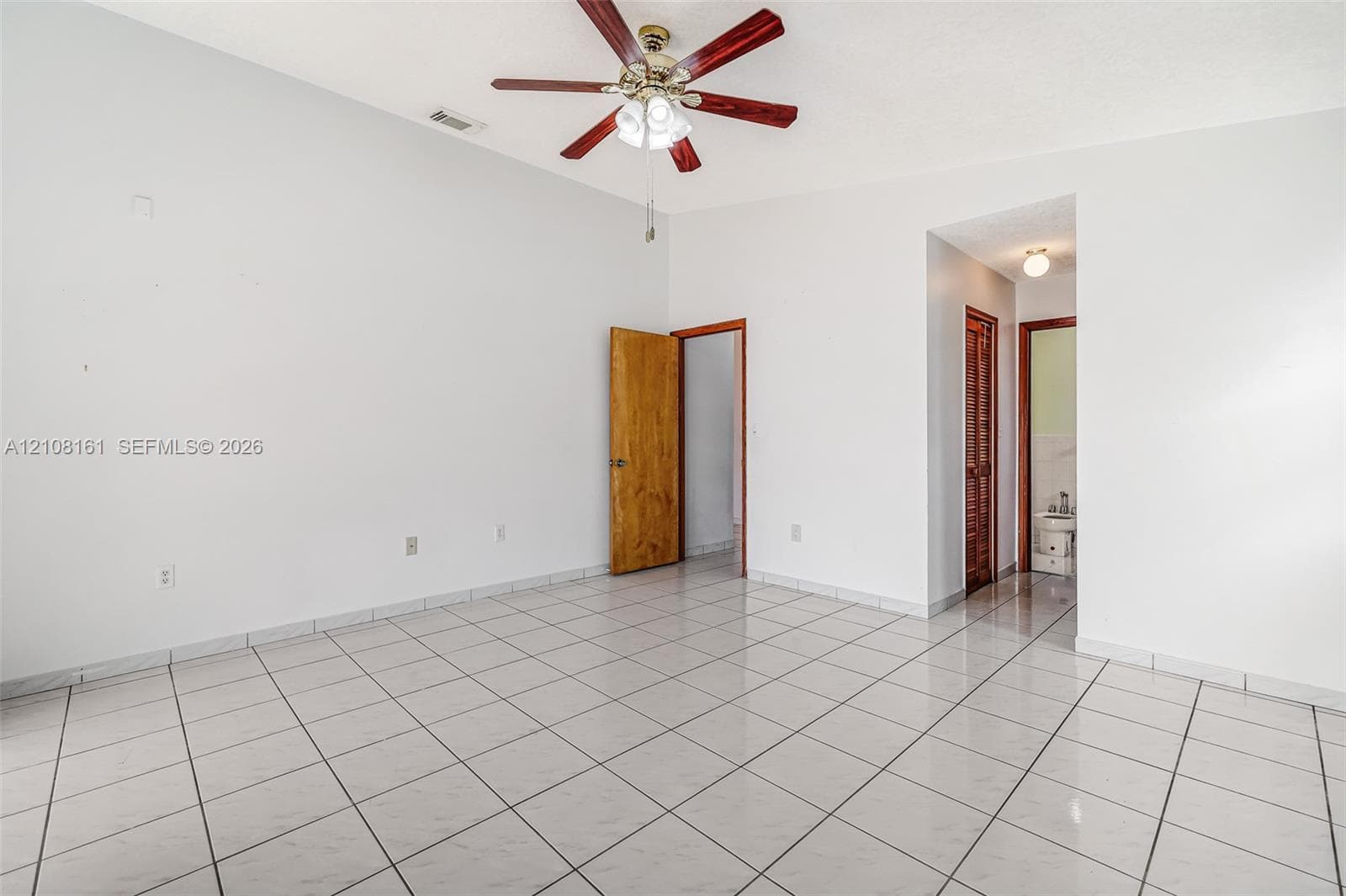Spacious room featuring vaulted ceilings, light-toned ceramic tile flooring, a multi-blade ceiling fan with integrated lighting, and wooden door finishes