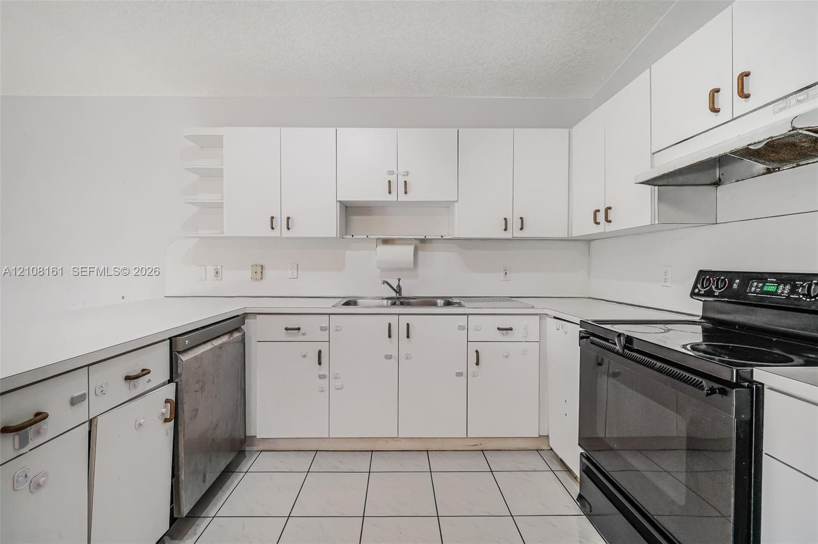 Kitchen featuring white cabinetry, solid-surface countertops, dual-basin stainless steel sink, tile flooring, and integrated black appliance suite