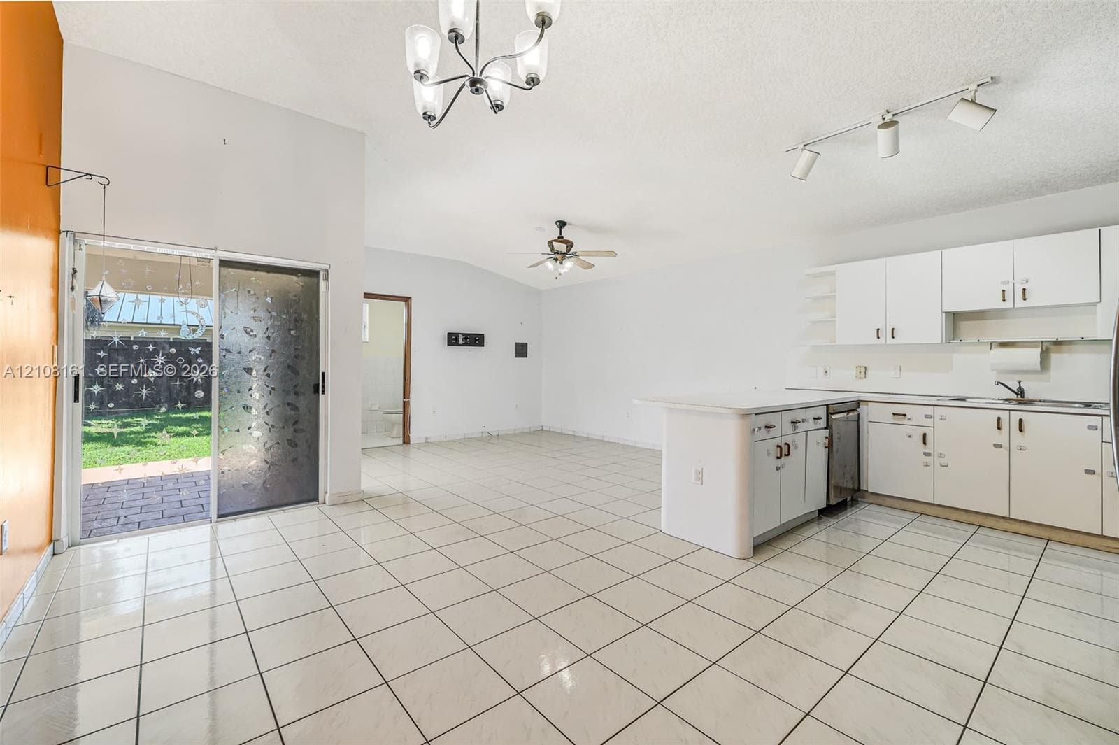 Open-concept kitchen featuring a center island, white cabinetry, tile flooring, sliding glass door, and vaulted ceilings with multi-bulb fixtures