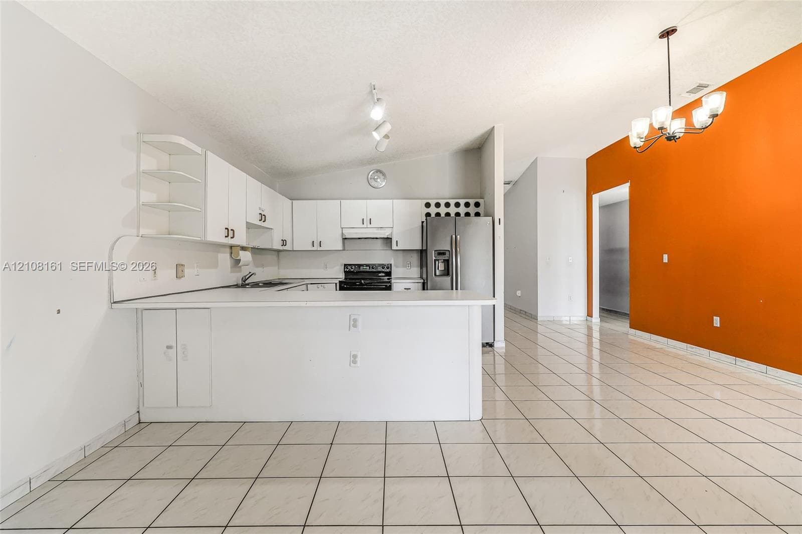 Kitchen featuring white cabinetry, a peninsula, stainless steel refrigerator, white countertops, and tile flooring
