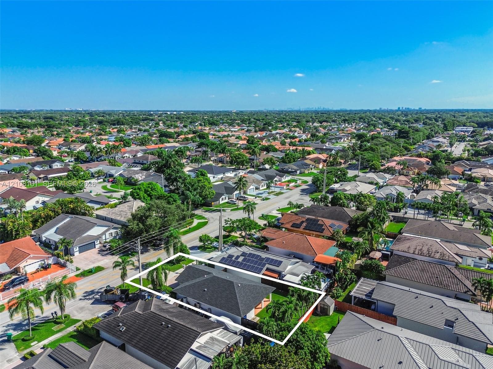 Aerial perspective of a single-story residence featuring a dark shingle roof, integrated solar panels, a fenced backyard, and established perimeter landscaping