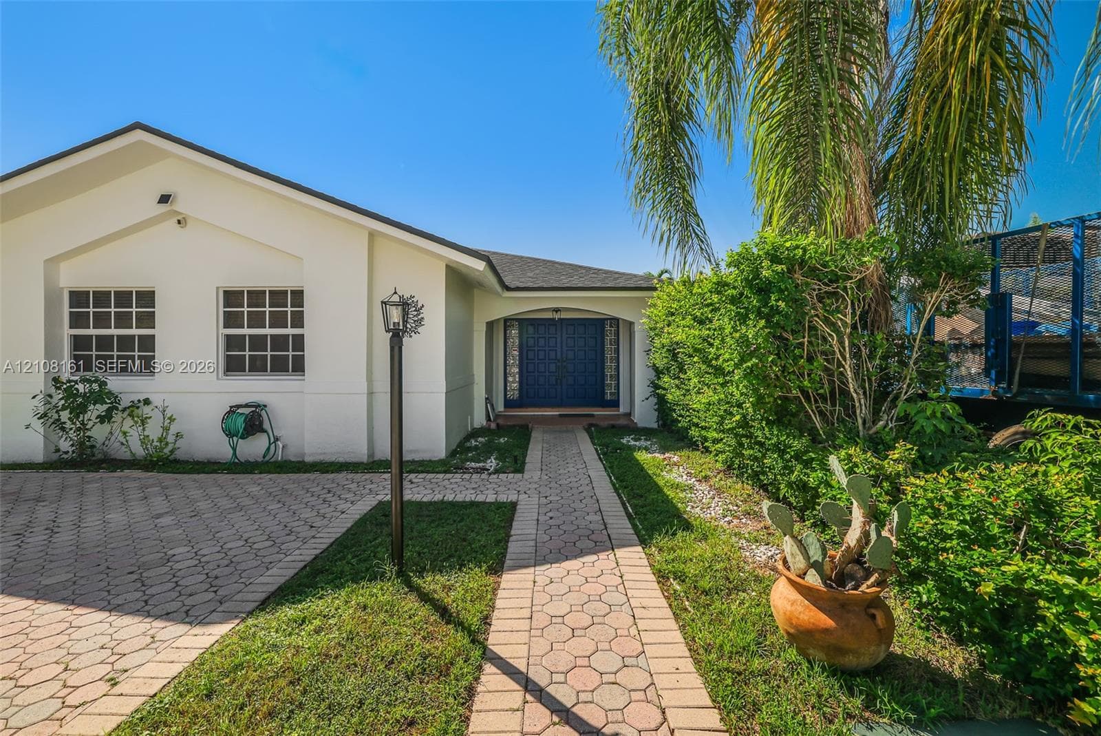 Single-story exterior featuring a light-toned stucco façade, decorative double-entry doors, a paver driveway, and a paved walkway