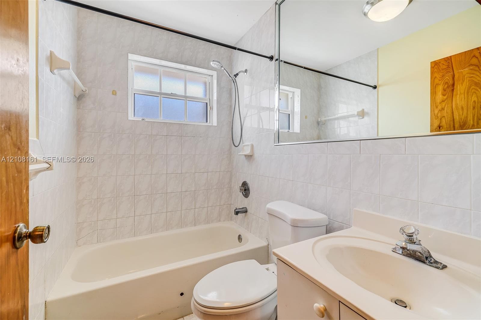 Bathroom featuring full-height wall tile, a standard tub and shower combination with chrome fixtures, a white vanity with an integrated sink, and a large-format vanity mirror