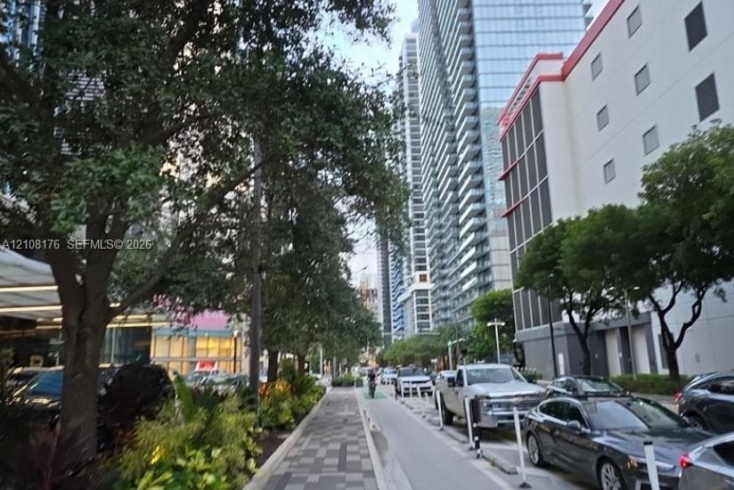 Urban streetscape featuring patterned paver walkways, mature canopy trees, and high-rise glass-façade architecture