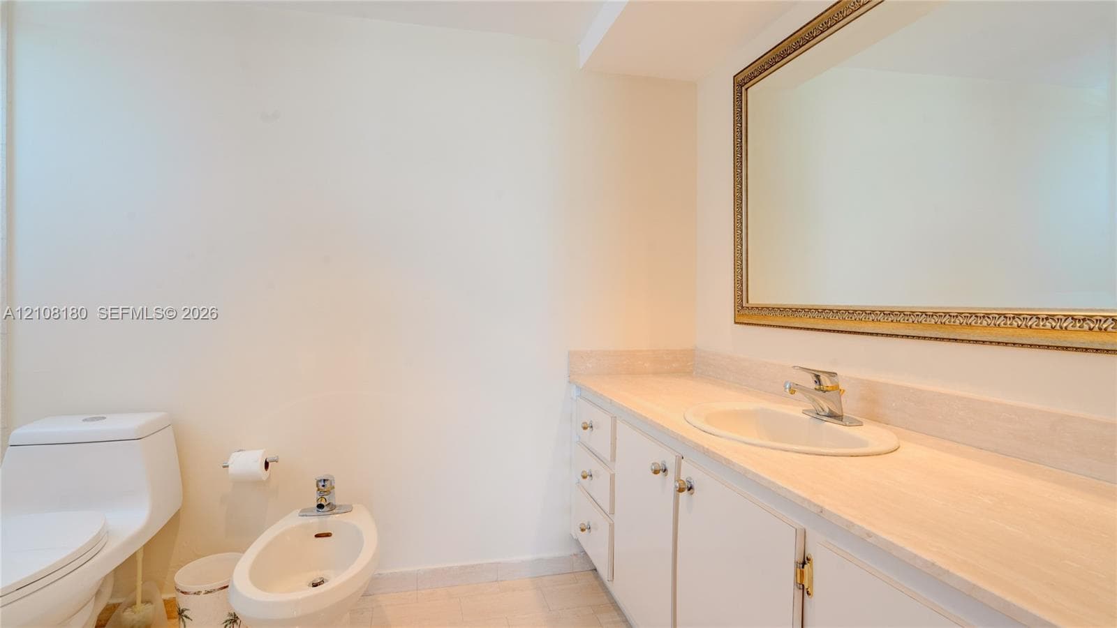 Bathroom featuring a neutral stone-finish countertop, white cabinetry with integrated storage, an oval undermount sink with a chrome faucet, a floor-mounted bidet, and a large wall-mounted mirror with a decorative frame
