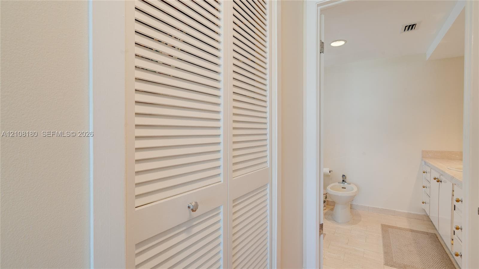 White louvered bifold closet doors featuring polished hardware, integrated white cabinetry with flat-panel drawers, and tile flooring