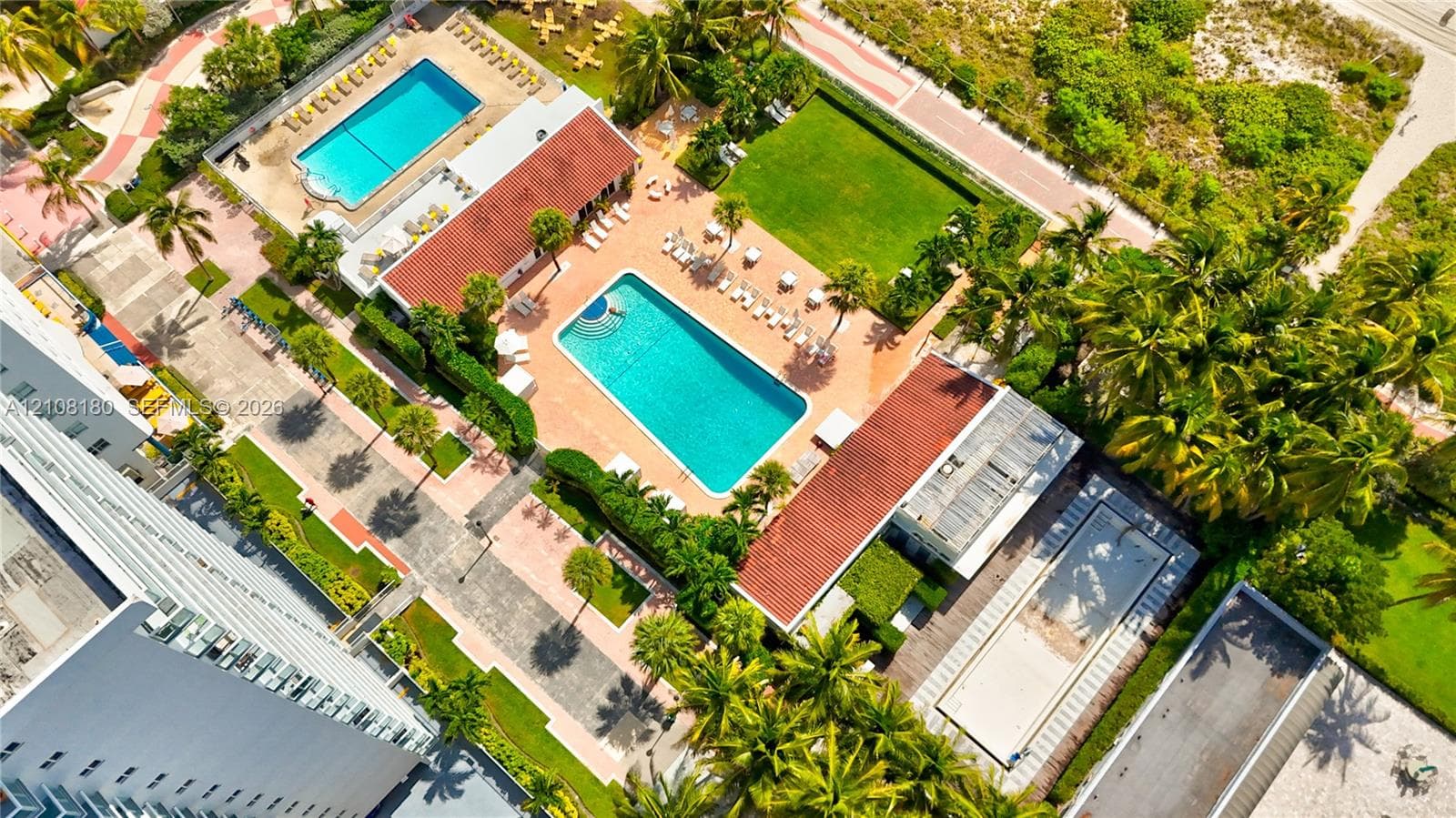 Aerial perspective of the grounds featuring two outdoor swimming pools, manicured lawn space, paved walkways, and mature palm trees