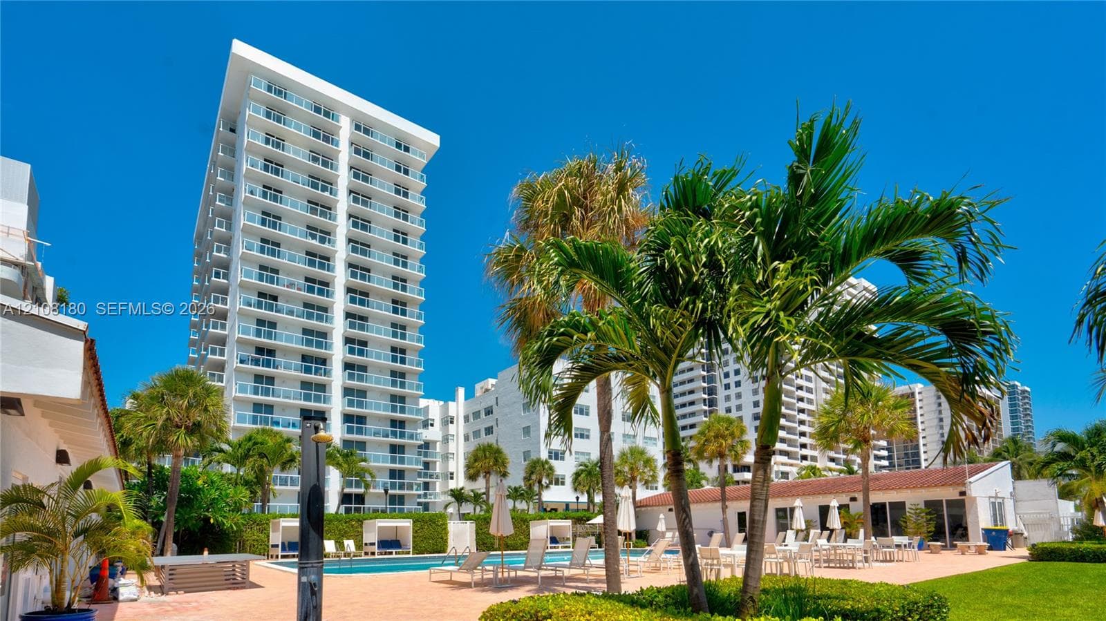 High-rise exterior featuring wraparound glass balconies, a swimming pool, paved pool deck, and landscaped palm trees