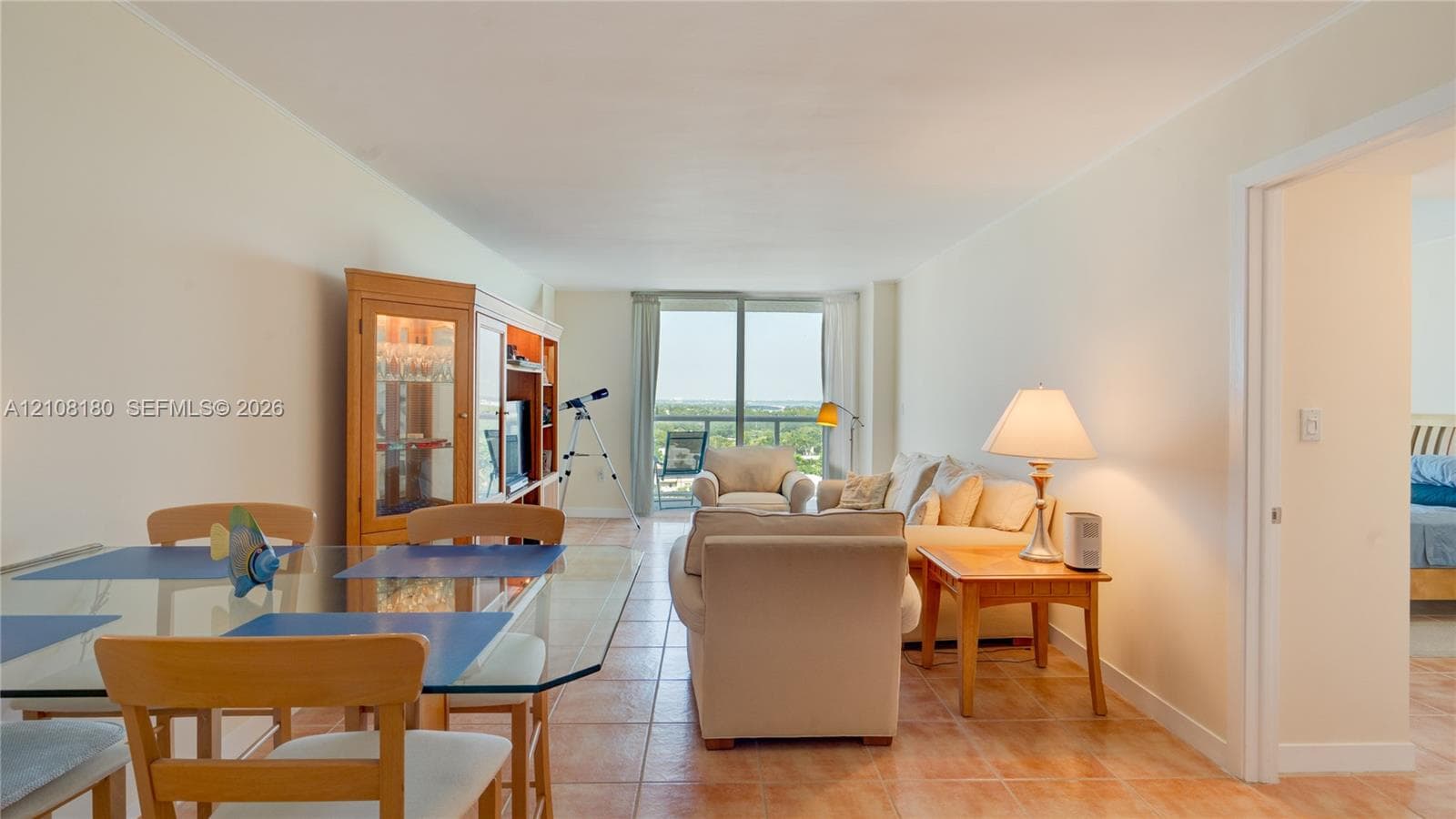 Open-concept interior featuring neutral wall tones, large-format tile flooring, and floor-to-ceiling glass doors leading to a private balcony