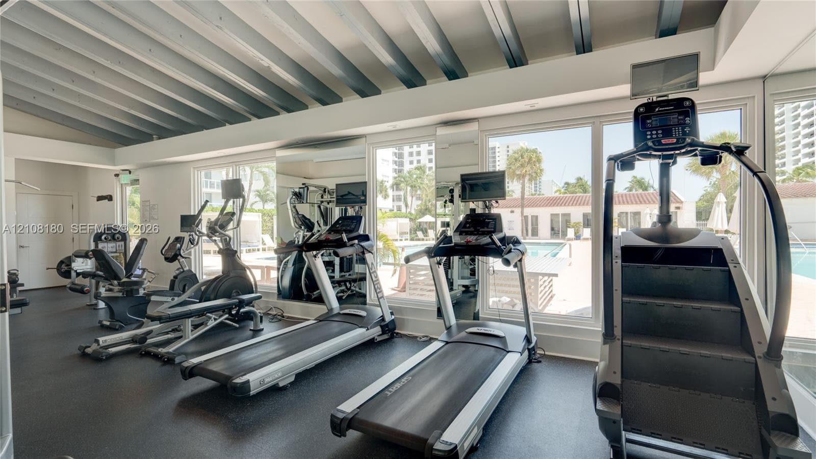 Fitness center featuring a vaulted ceiling with exposed beams, wall-to-wall mirrors, and floor-to-ceiling windows