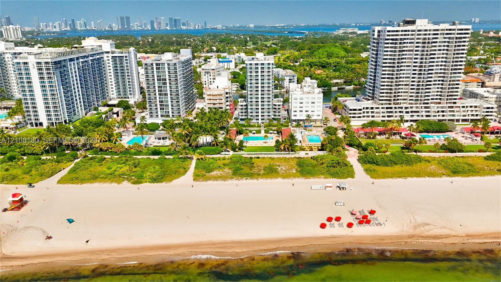 Aerial perspective of oceanfront property featuring sandy beach access, mature tropical landscaping, and outdoor swimming pools