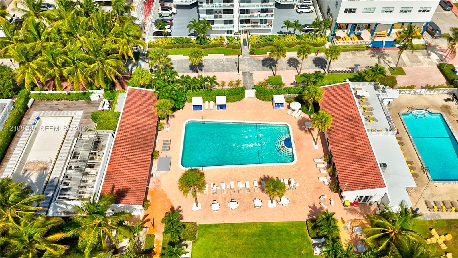 Aerial perspective of a multi-pool courtyard featuring terracotta-tiled roofs, manicured lawns, mature palm trees, and paved deck surfaces