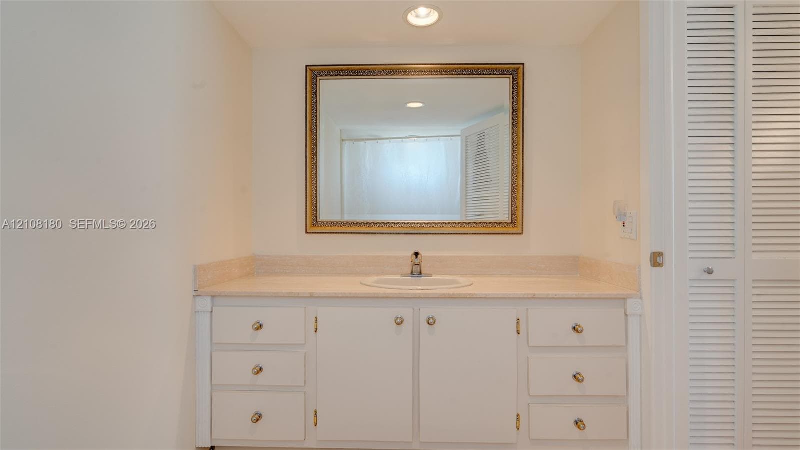 Vanity featuring a stone countertop, integrated sink, white cabinetry with metallic hardware, and a framed wall-mounted mirror