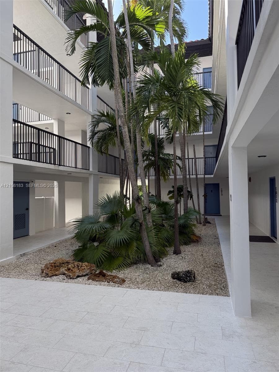 Central courtyard featuring stone-paved walkways, mature palm trees, decorative rock landscaping, and multi-level balconies with black metal railings