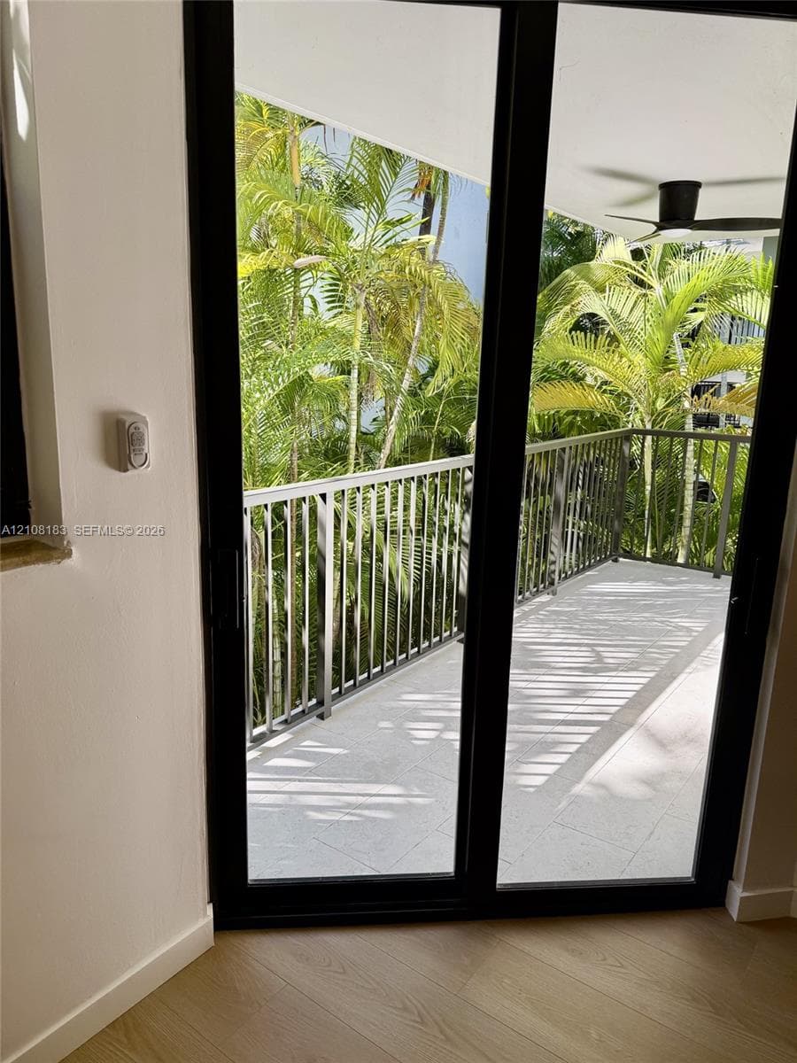Covered balcony featuring black metal railings, large-format tile flooring, a ceiling fan, and mature palm trees