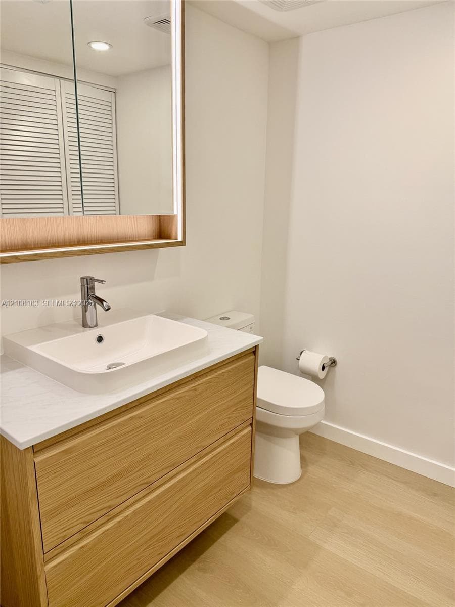 Floating wood-finish vanity with a rectangular sink, stone-composite countertop, integrated LED-lit medicine cabinet, and wood-finish flooring
