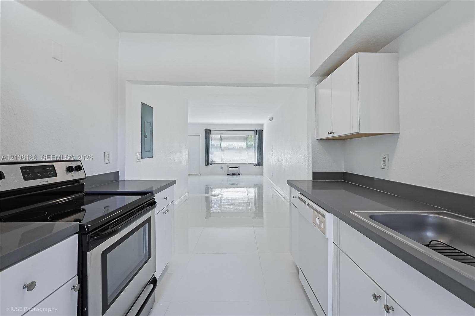 Kitchen featuring white cabinetry, solid-surface countertops, stainless steel electric range, built-in dishwasher, and large-format tile flooring