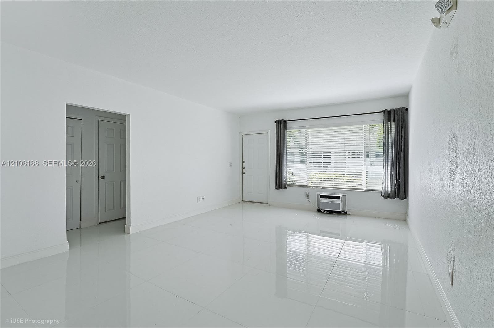 Bright interior space featuring polished tile flooring, a large picture window with horizontal blinds, and a wall-mounted air conditioning unit