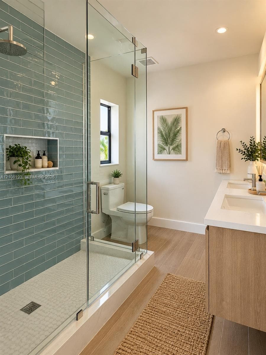 Walk-in shower featuring a frameless glass enclosure, blue subway tile surround, and built-in recessed niche, paired with a dual-sink vanity and wood-finish flooring