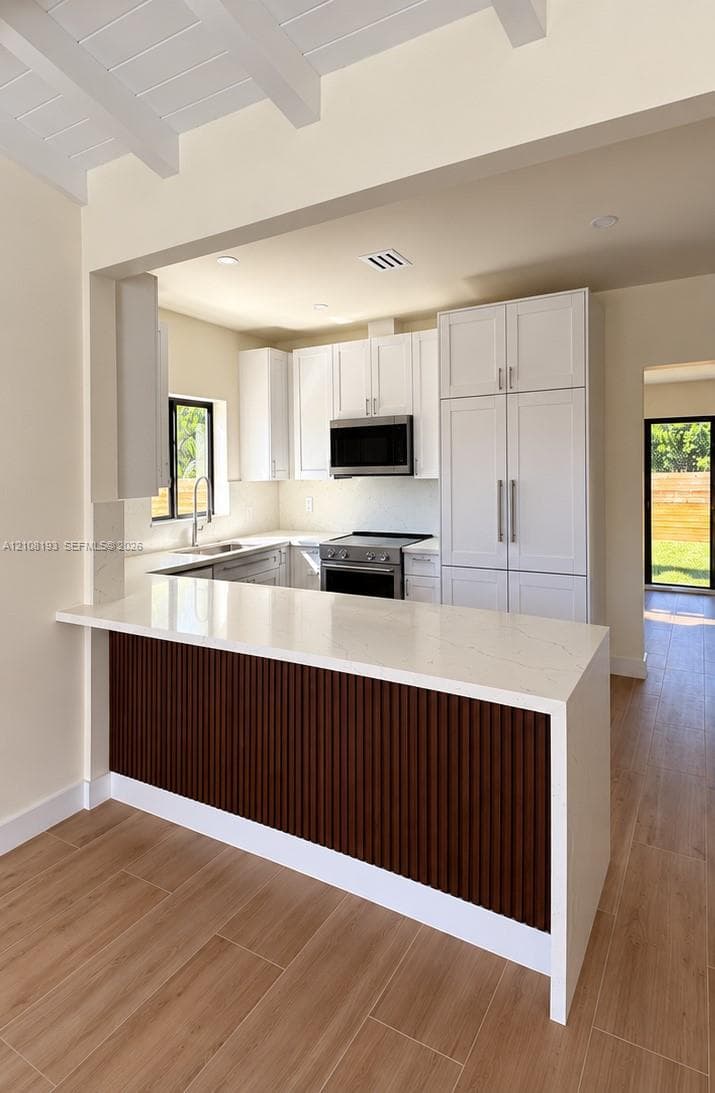 Kitchen featuring white cabinetry, wood-finish flooring, a waterfall edge countertop, a slatted wood-paneled island, and recessed ceiling beams