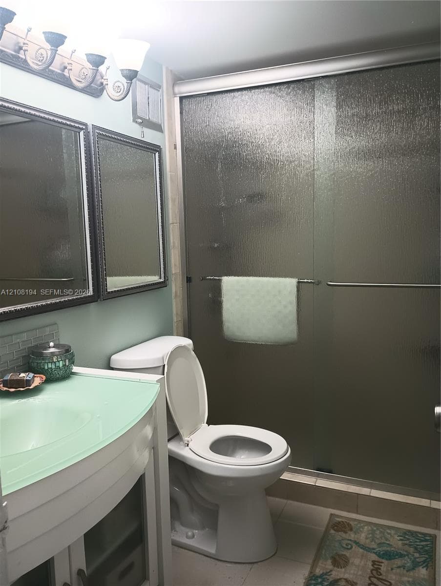 Bathroom featuring a vanity with a translucent green countertop, dual framed wall-mounted mirrors, a multi-light fixture, and a walk-in shower with textured glass sliding doors