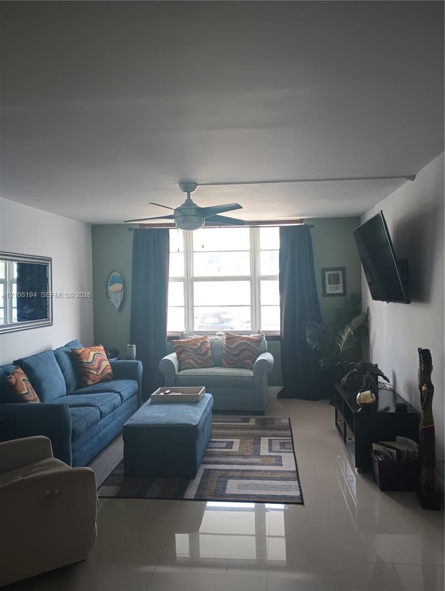 Living area featuring large format tile flooring, multi-pane window with central mullions, and a ceiling-mounted fan with integrated light fixture