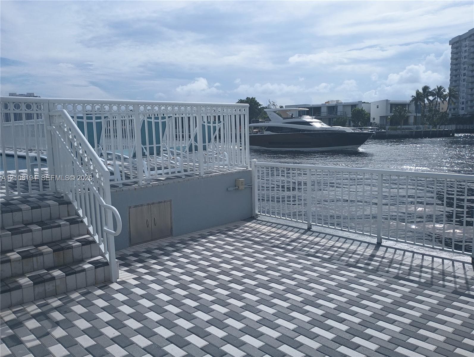 Waterfront terrace featuring multi-tone paved surfacing, white aluminum railings, built-in storage cabinet, and elevated staircase