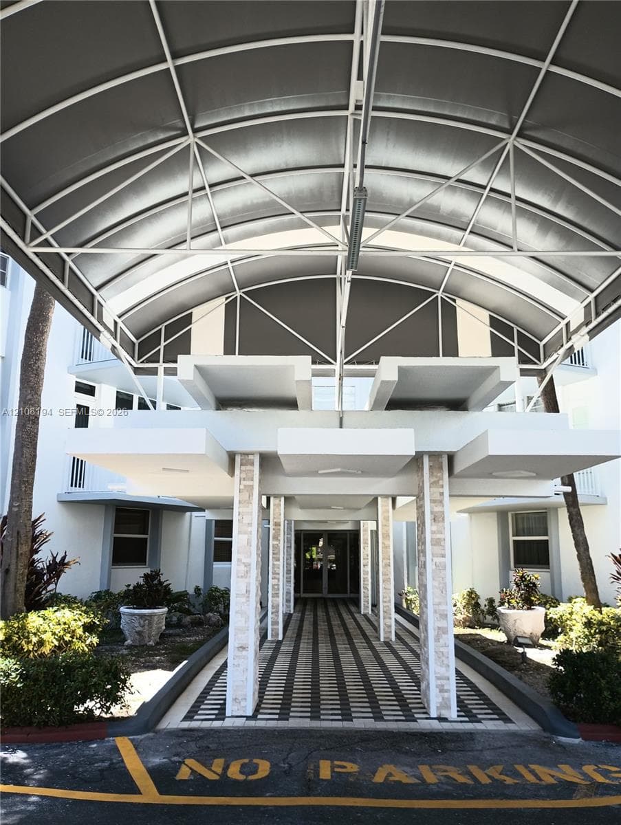 Covered building entrance featuring an arched metal portico, geometric stone-clad pillars, and a multi-toned paved walkway