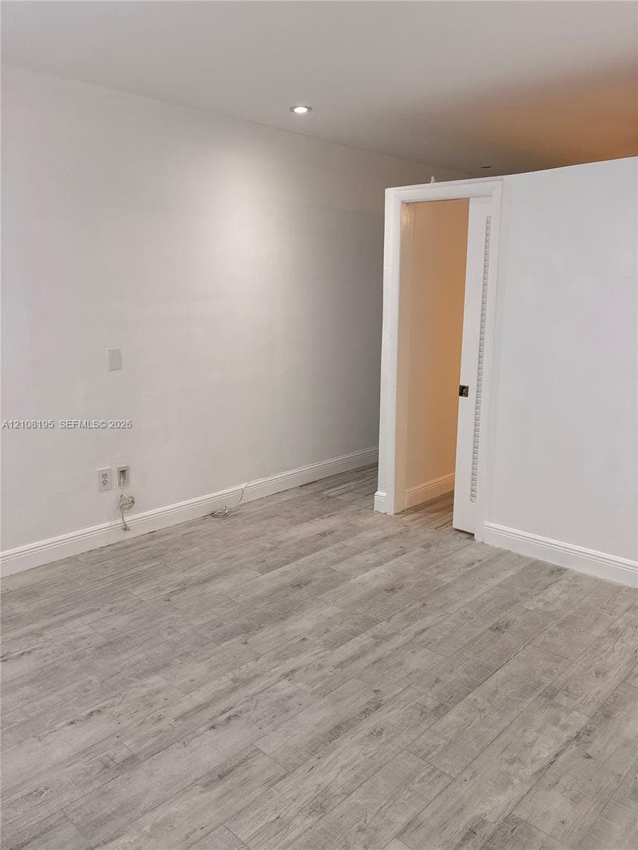 Interior space featuring wood-finish flooring, recessed ceiling lighting, and a white interior door with a louvered panel
