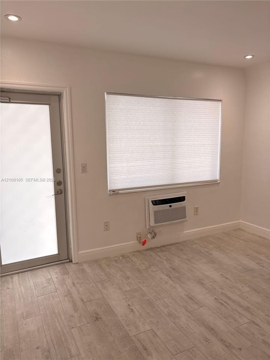 Wood-finish tile flooring, recessed ceiling lighting, glass-panel entry door, and wall-mounted air conditioning unit