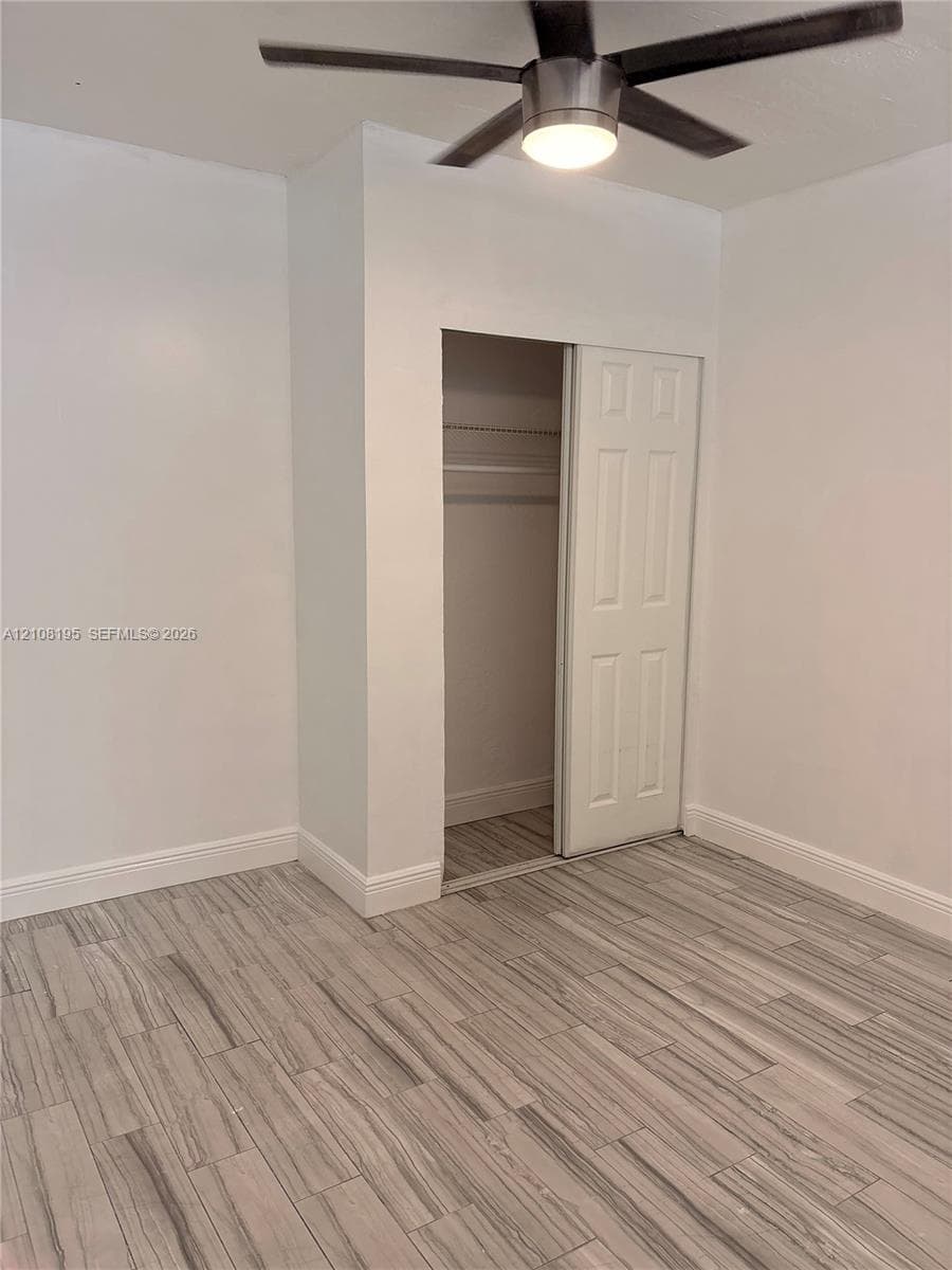 Room featuring wood-finish tile flooring, a neutral color palette, a ceiling fan with integrated lighting, and a closet with a paneled sliding door