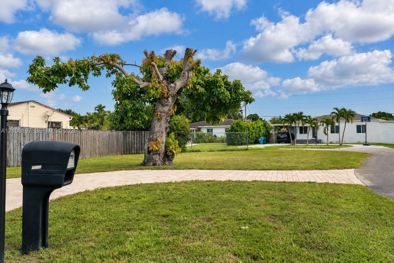 Expansive front yard featuring paver walkway, mature tree, and perimeter wood fencing