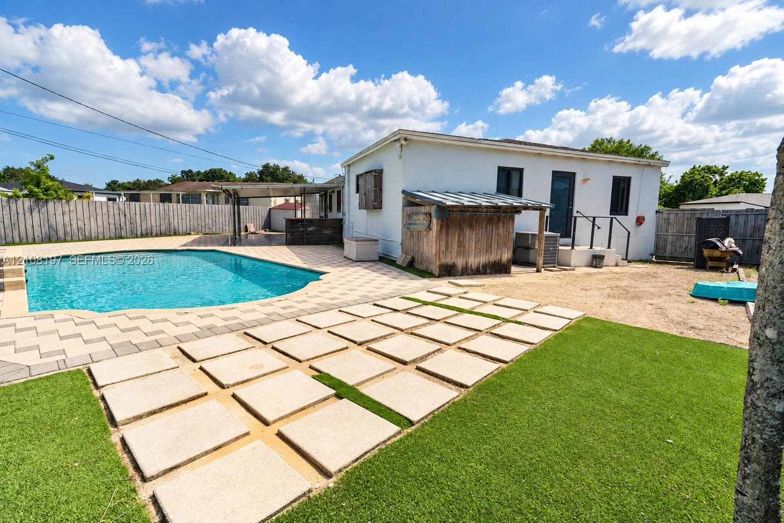Backyard featuring an in-ground swimming pool, concrete paver patio, synthetic turf lawn, wood privacy fencing, and a built-in outdoor structure