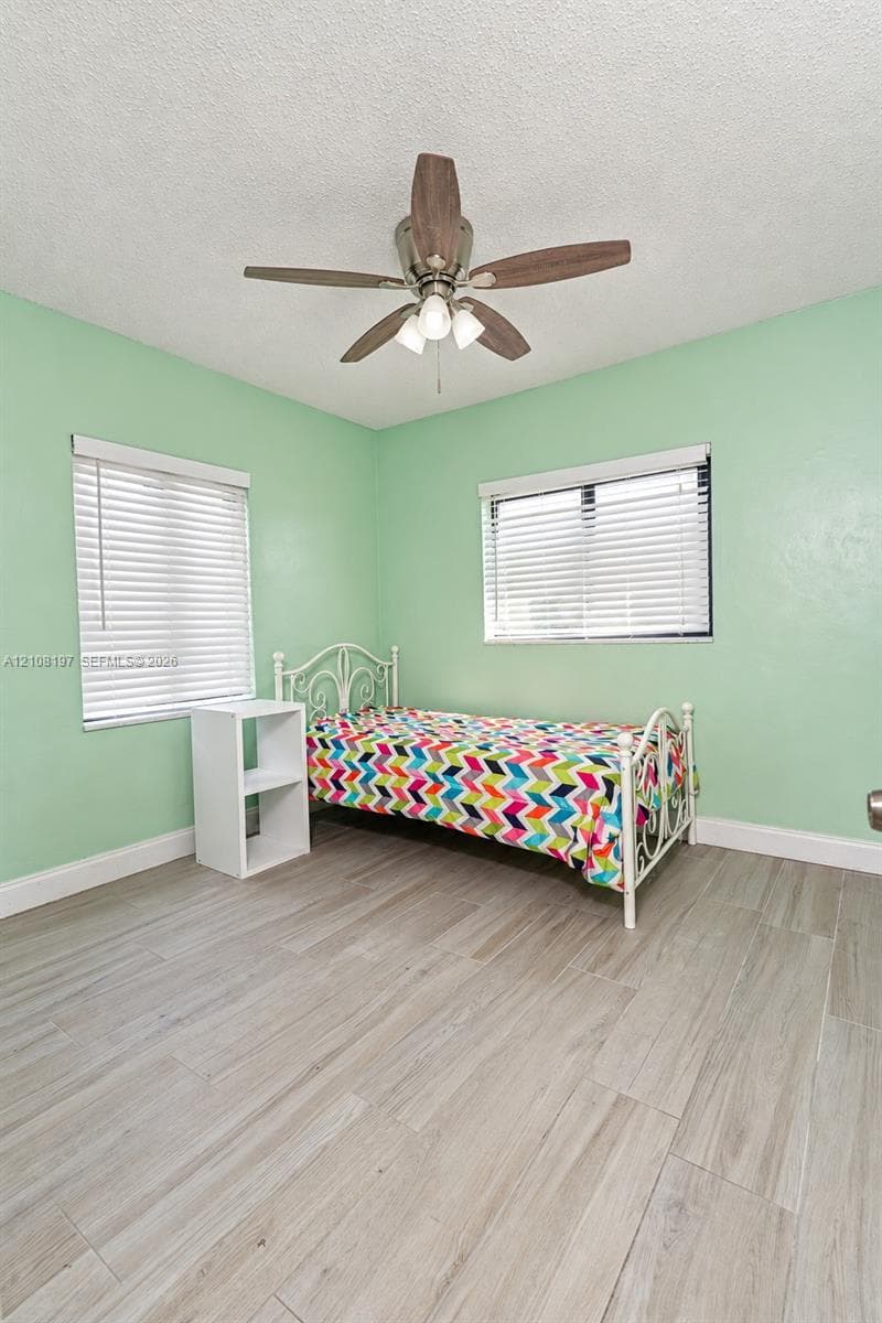 Room featuring wood-finish tile flooring, two windows with horizontal blinds, and a ceiling fan with integrated light fixture