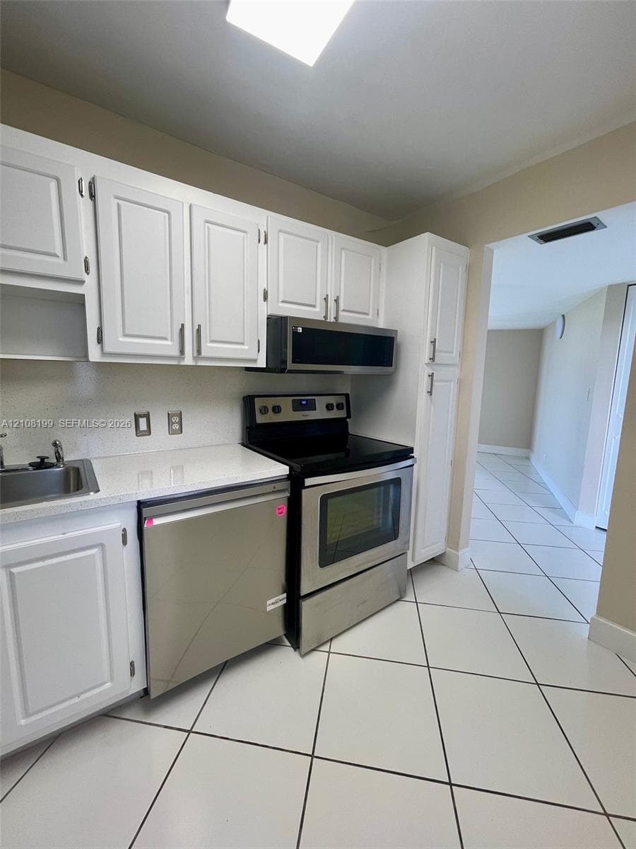 Kitchen featuring white cabinetry, stone-finish countertops, stainless steel appliances, and tile flooring