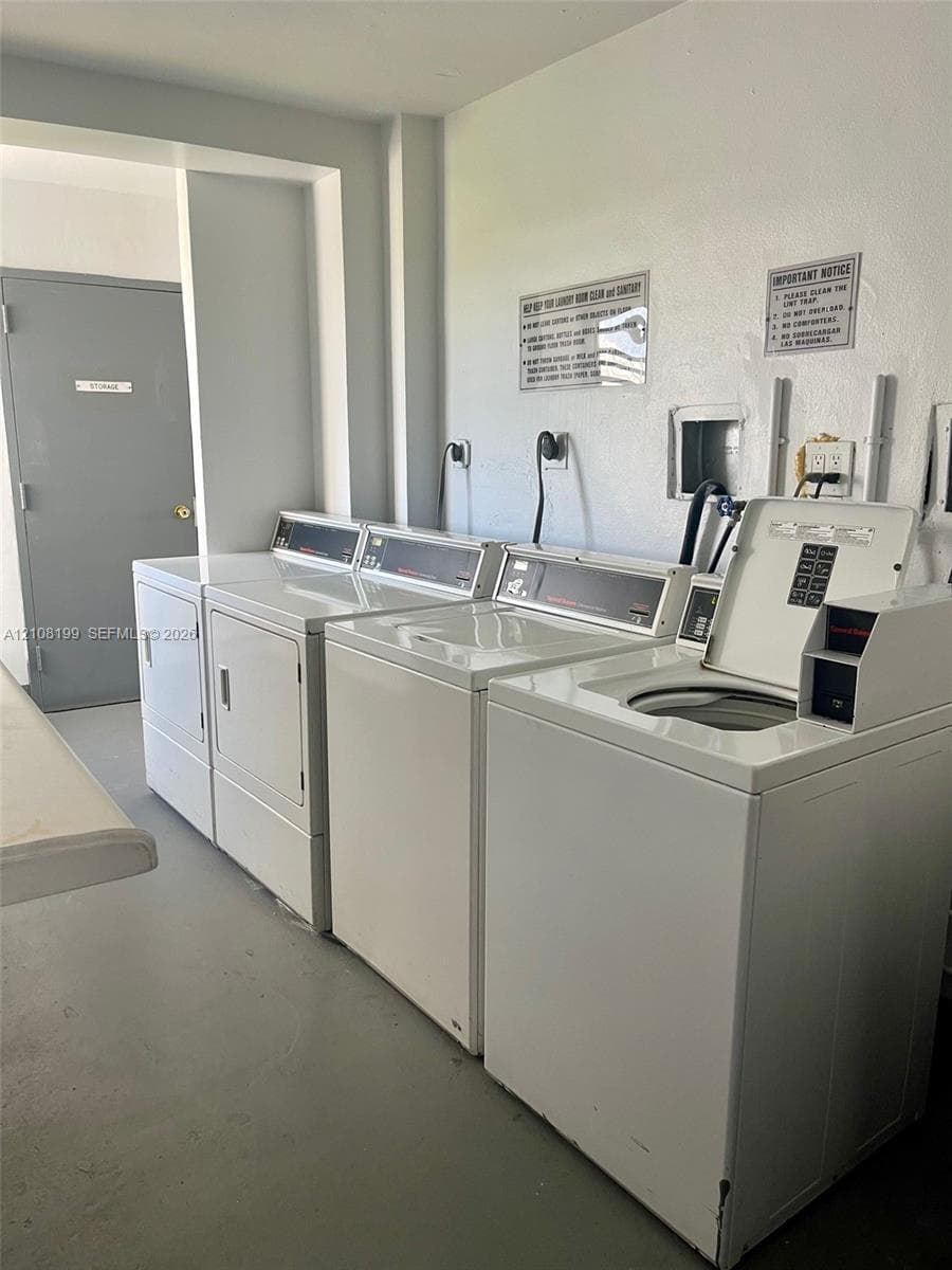 Laundry facility featuring multiple top-load washers and front-load dryers, solid-surface flooring, and a grey flush-panel door