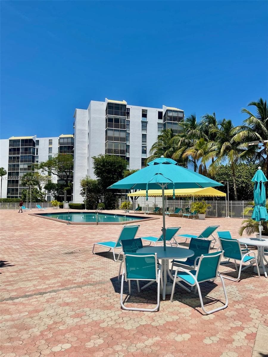Outdoor swimming pool surrounded by a paved deck featuring mature palm trees and perimeter fencing