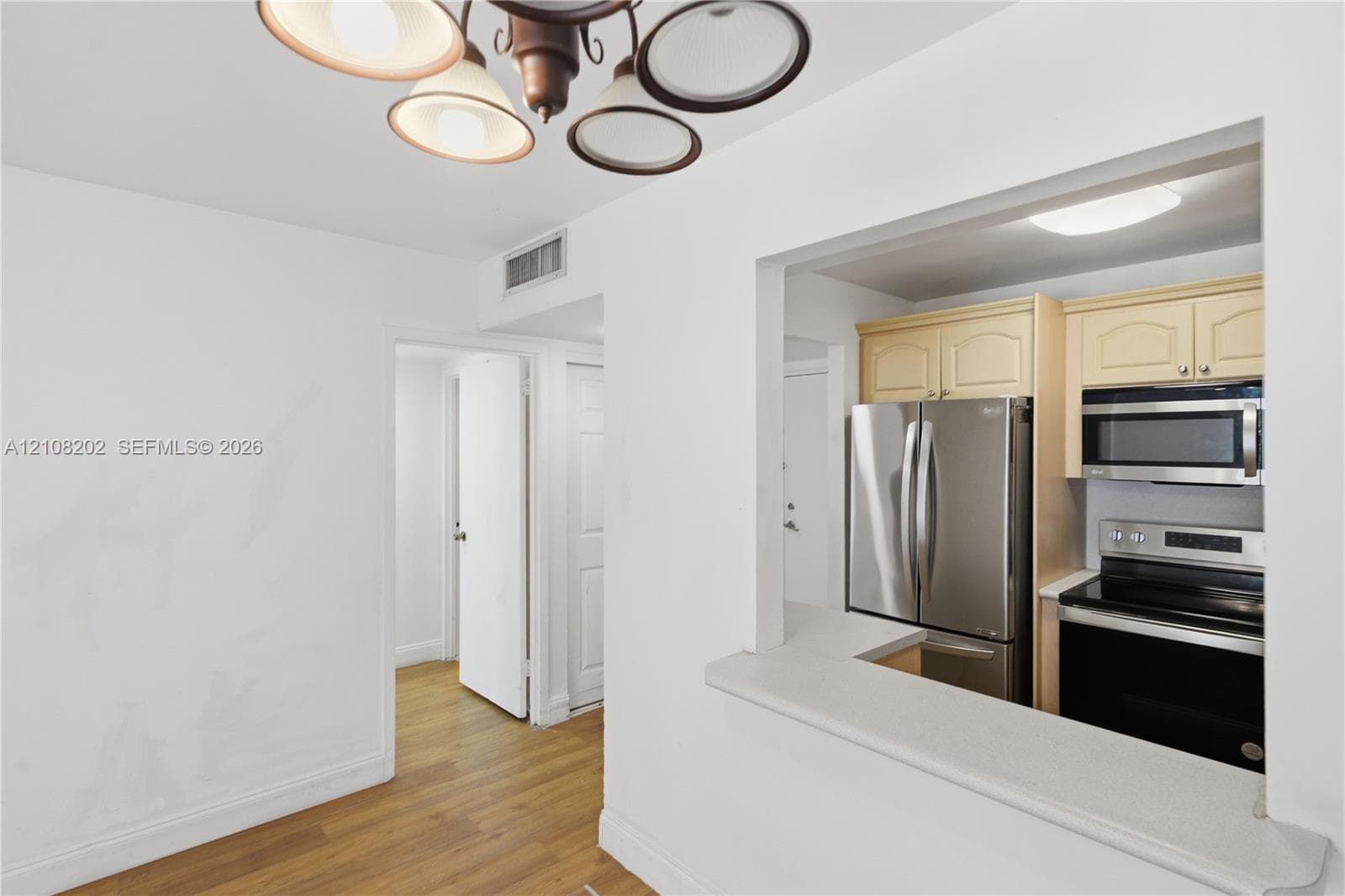 Kitchen featuring a pass-through opening, stone-finish countertops, stainless steel appliances, wood-finish flooring, and a multi-light chandelier