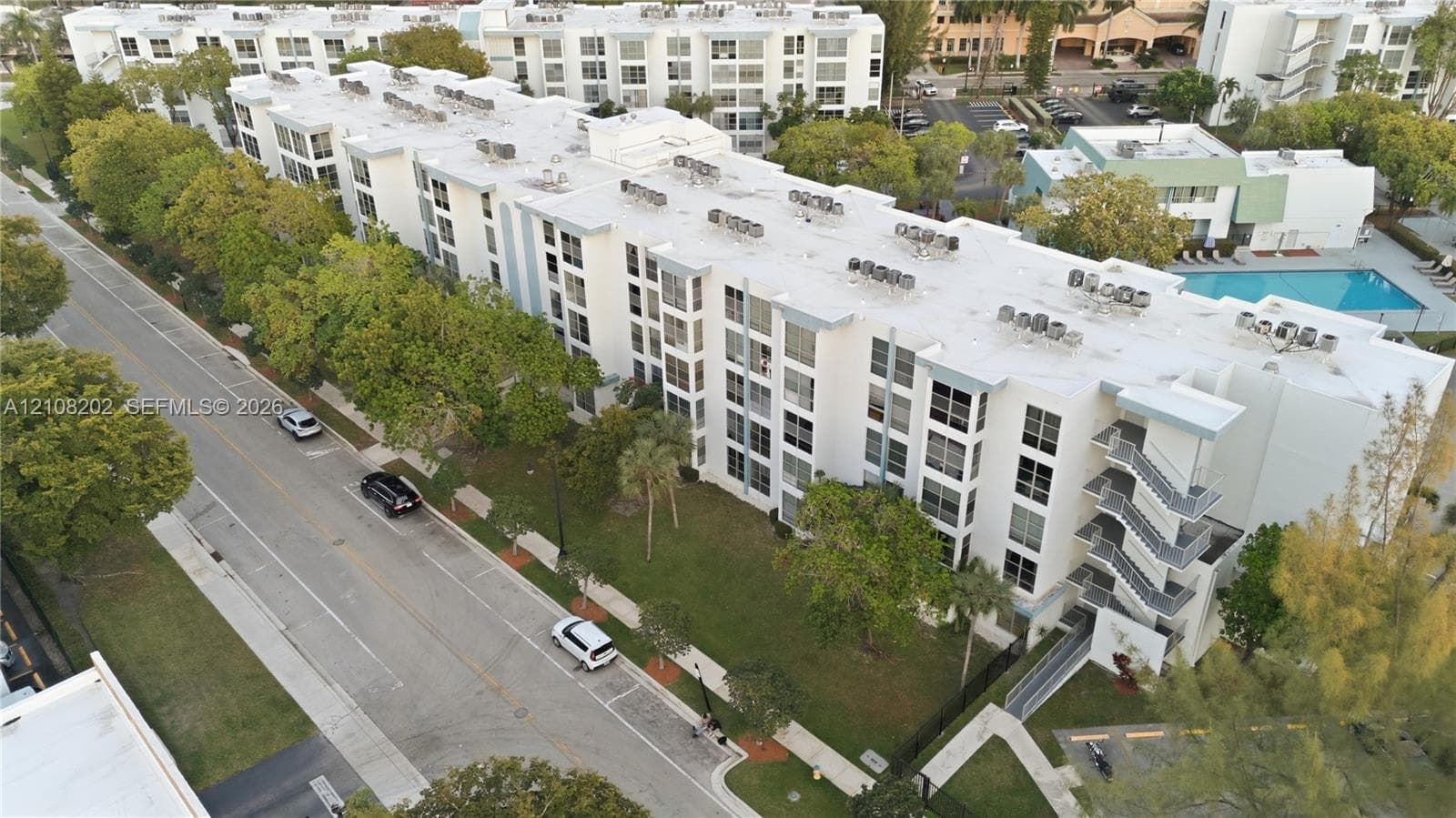 Multi-story building exterior featuring a white facade, structured metal stairwells, flat roofing, and an onsite swimming pool