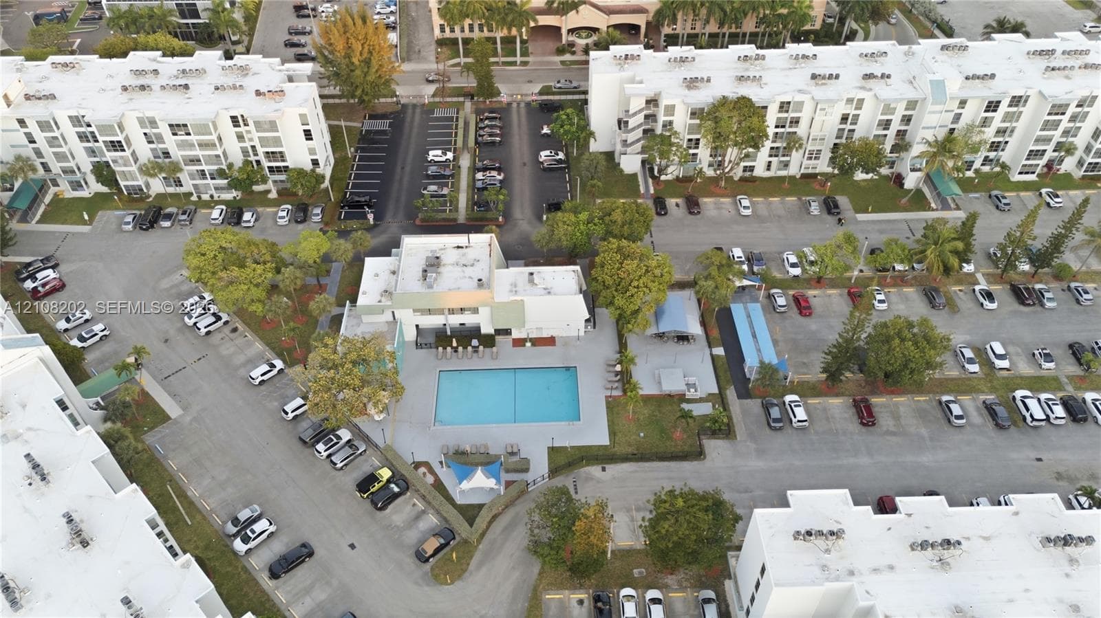 Aerial perspective of a multi-unit complex featuring an outdoor swimming pool, paved surface parking areas, and mature landscaping
