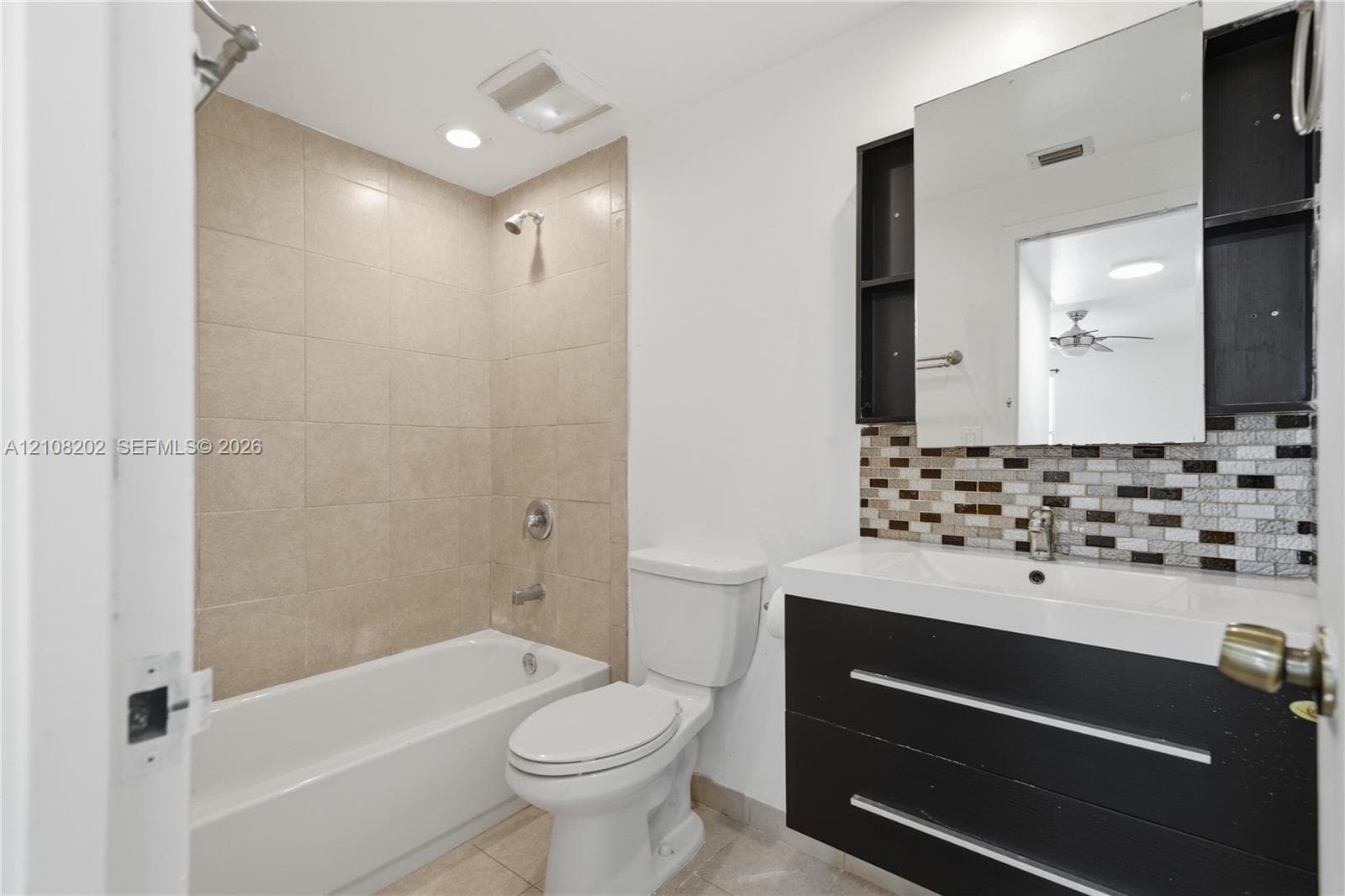 Bathroom featuring a floating dark-finish vanity with an integrated basin, multi-toned mosaic tile backsplash, medicine cabinet, and a bathtub with beige wall tiling