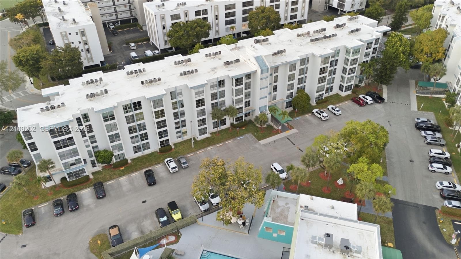 Multi-story residential building featuring a flat roof, concrete exterior, dedicated surface parking, and manicured landscaping