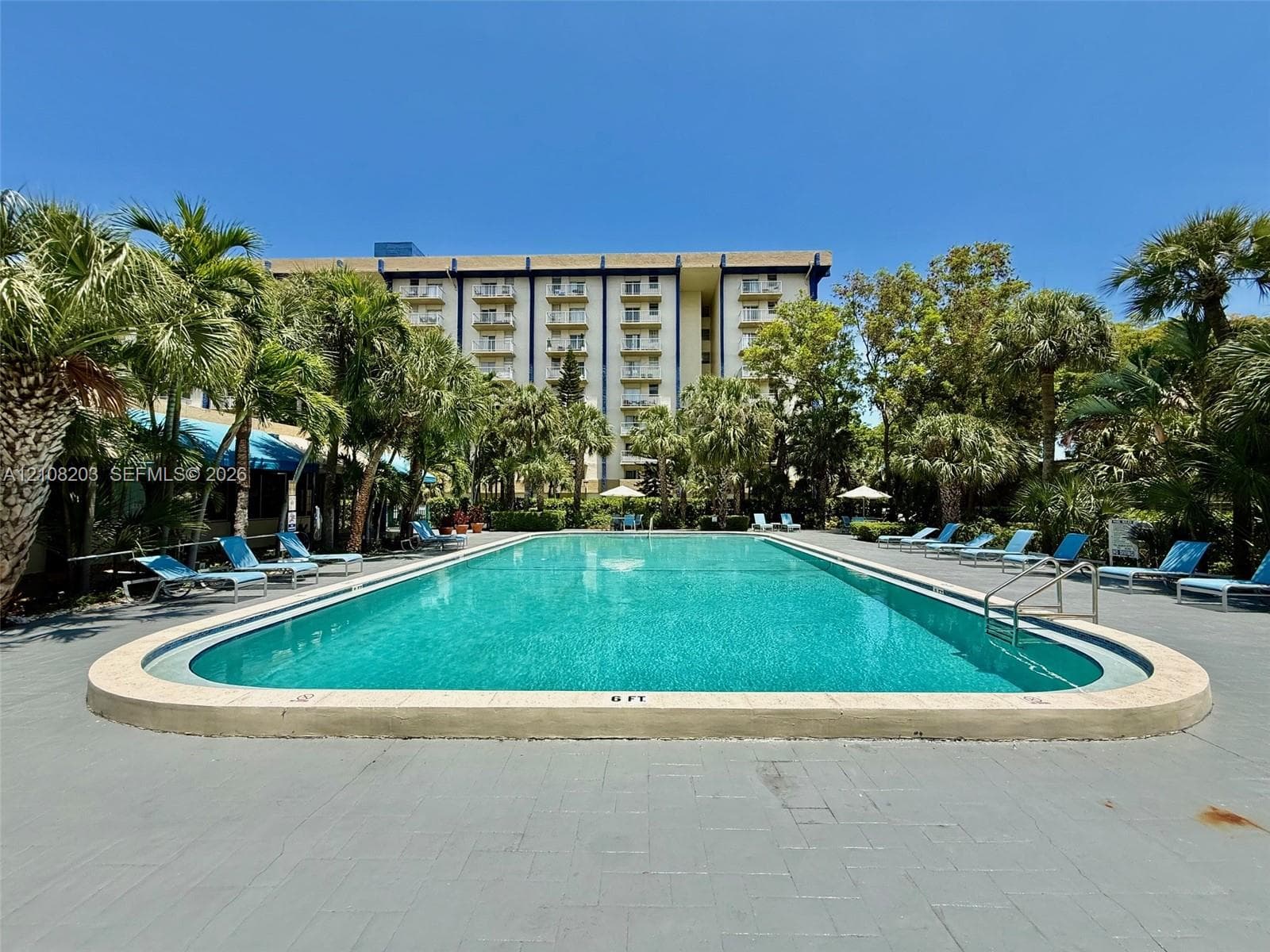 Outdoor swimming pool featuring a concrete deck, built-in metal handrails, and surrounding palm trees