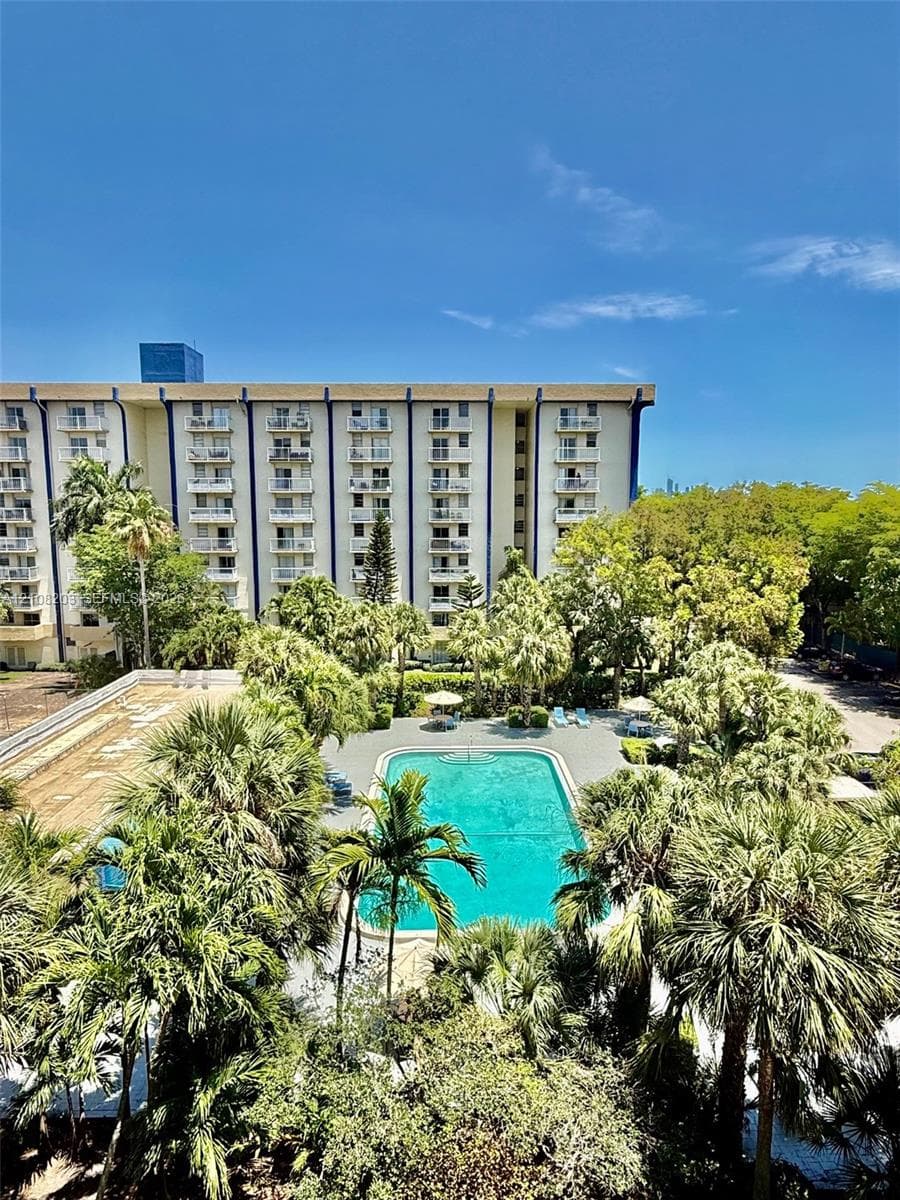 Multi-story residential building featuring private balconies, rectangular swimming pool, and extensive mature tropical landscaping