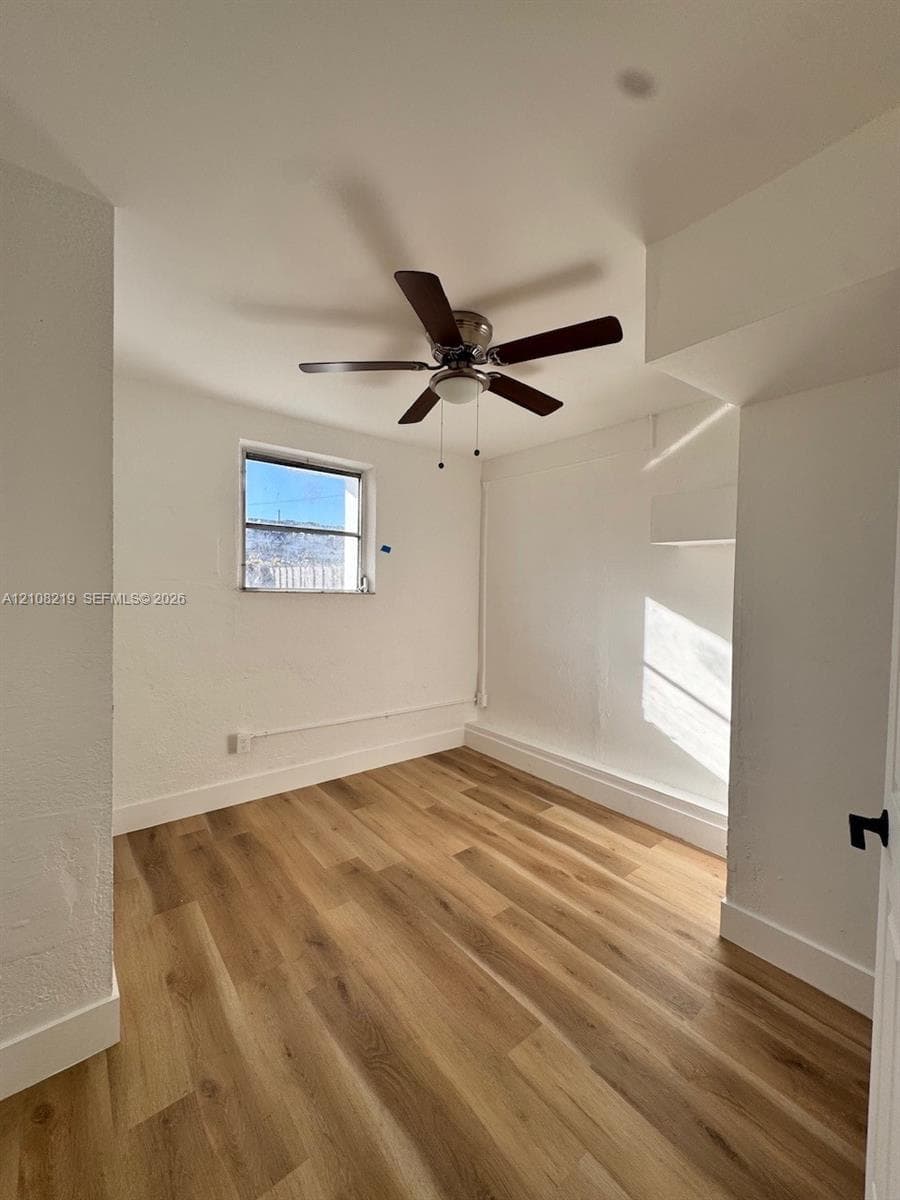Interior space featuring wood-finish flooring, white walls, and a ceiling-mounted fan with integrated light fixture